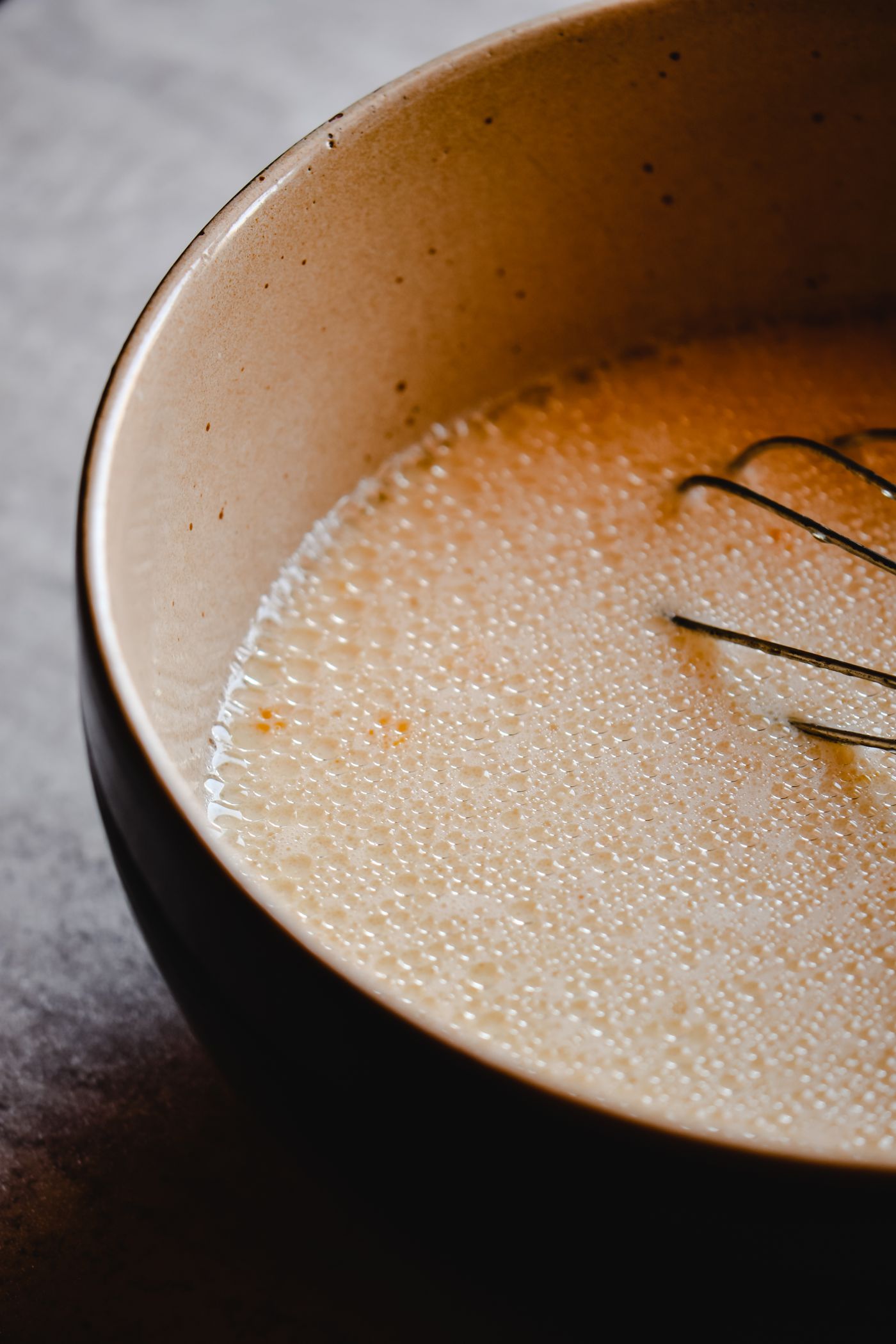 Bubbly waffle batter in a ceramic bowl with a whisk