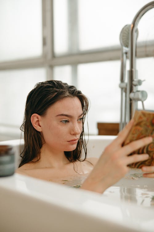 Free Woman Reading a Book While in a Bathtub Stock Photo