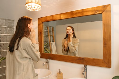 Free Woman Applying Cosmetic Product on Her Face While Looking at Mirror Stock Photo