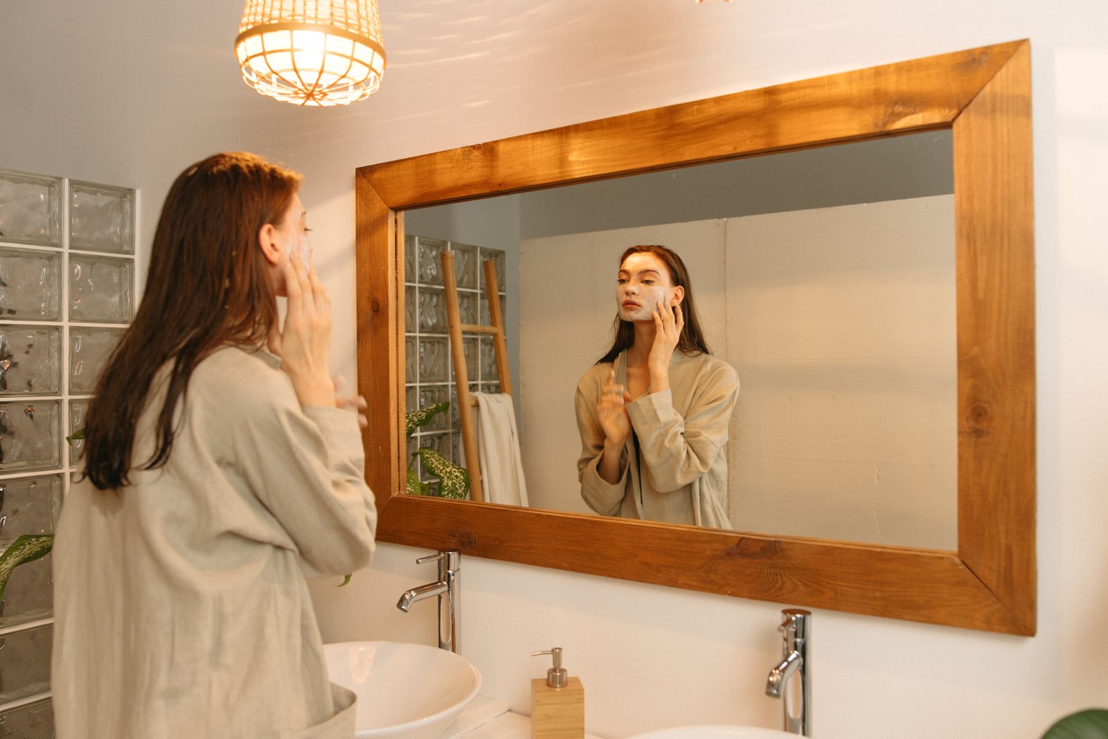 Woman applying skincare cream while checking her face in a bathroom mirror