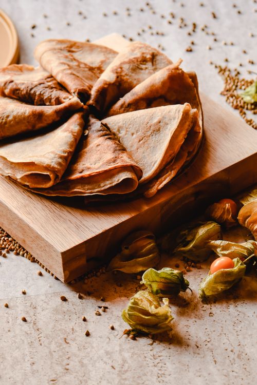 Free Close-up shot of beautifully arranged crepes and physalis on a wooden board, perfect for food photography. Stock Photo