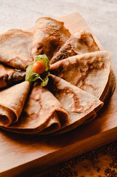 Close-up of golden brown crepes with a physalis garnish on a rustic wooden board.