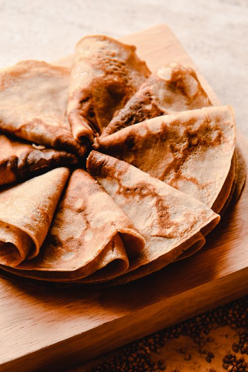 Free Close-up of freshly made crepes displayed on a wooden board, captured in warm and inviting tones. Stock Photo