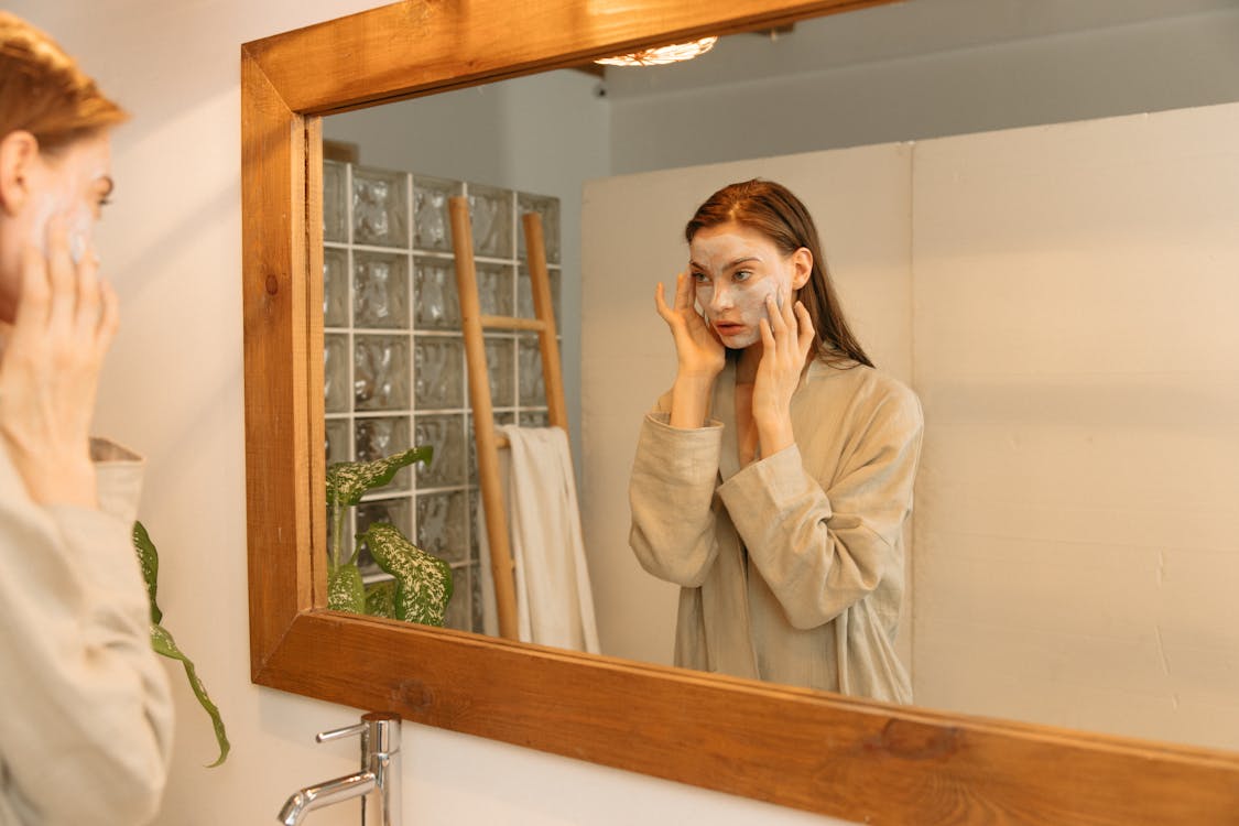 Free Person Applying Cosmetic Product on Her Face While Looking at the Mirror Stock Photo