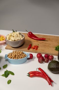 An arrangement of fresh ingredients including chickpeas, radishes, peppers, and tofu on a cutting board.