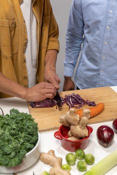 Close-up of hands slicing red cabbage, carrot, and ginger on a chopping board.