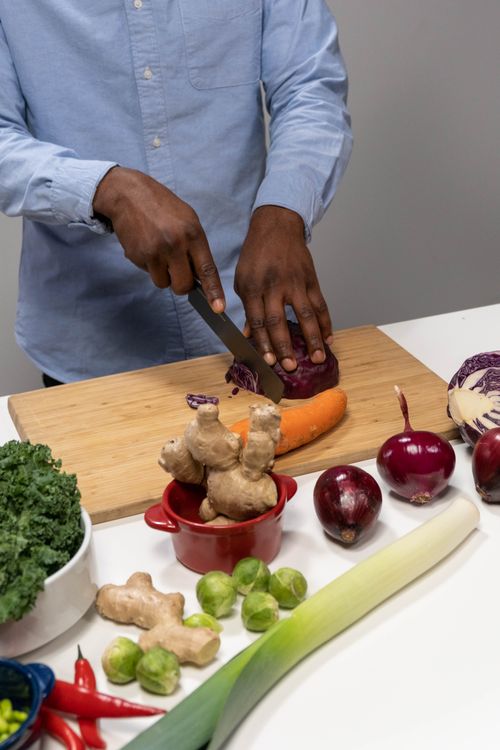 Free Person slicing fresh vegetables including red cabbage and carrots on a wooden board indoors. Stock Photo