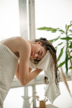 Relaxed woman drying her hair with a towel indoors, enjoying a moment of self-care.