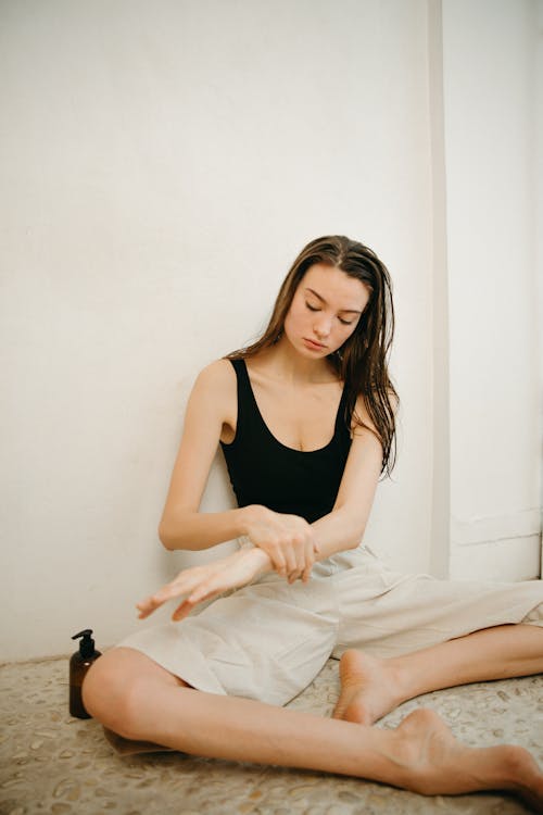 Free A Woman Sitting on the Floor while Applying Lotion on Her Arm Stock Photo