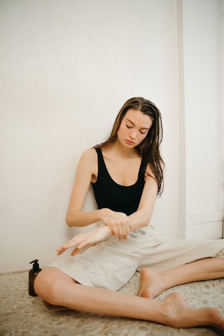 A Woman Sitting On The Floor While Applying Lotion On Her Arm