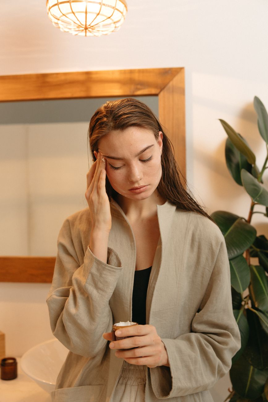 Young woman gently applying skincare cream in a peaceful indoor setting, enhancing her beauty routin