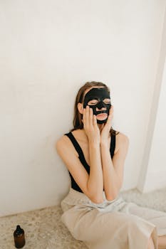 Woman applying a black facial mask for skincare and relaxation. Wellness routine indoors.