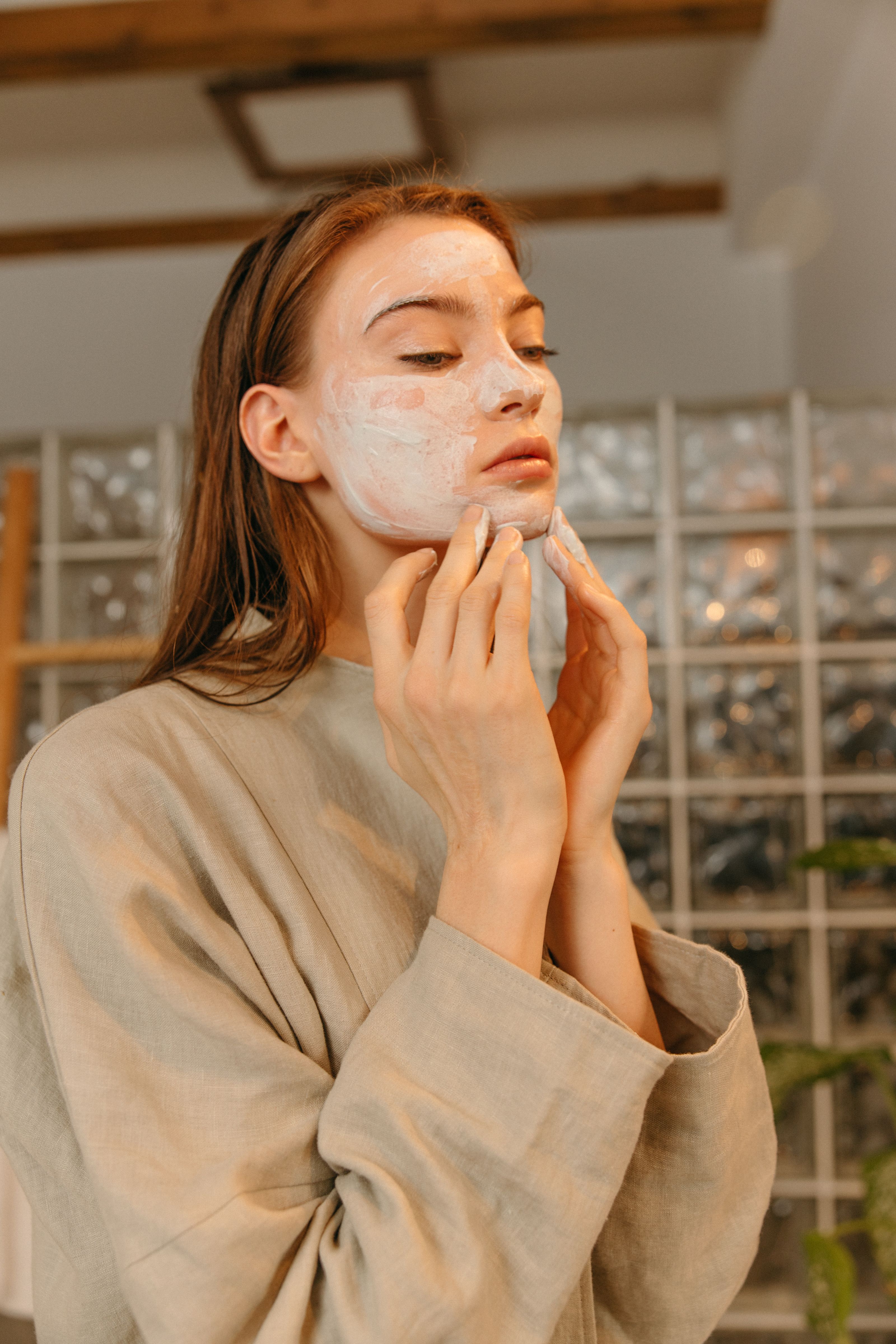 Uma mulher aplica uma máscara facial enquanto relaxa em casa para sua rotina de cuidados com a pele.