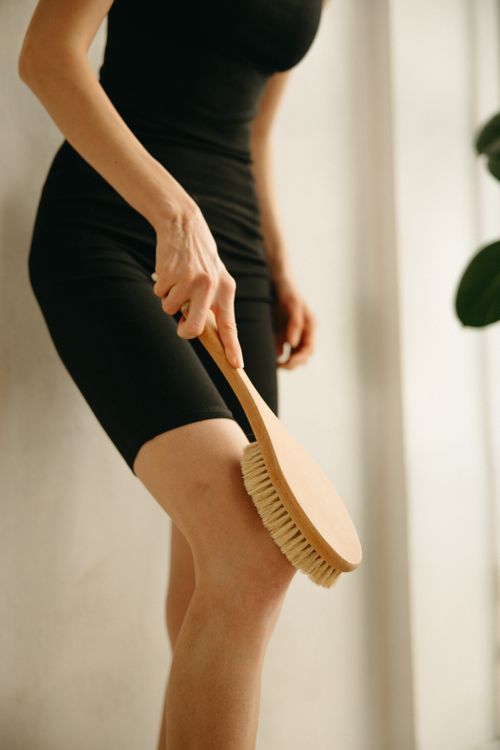Free A woman uses a wooden brush to exfoliate her leg, promoting skincare and wellness. Stock Photo