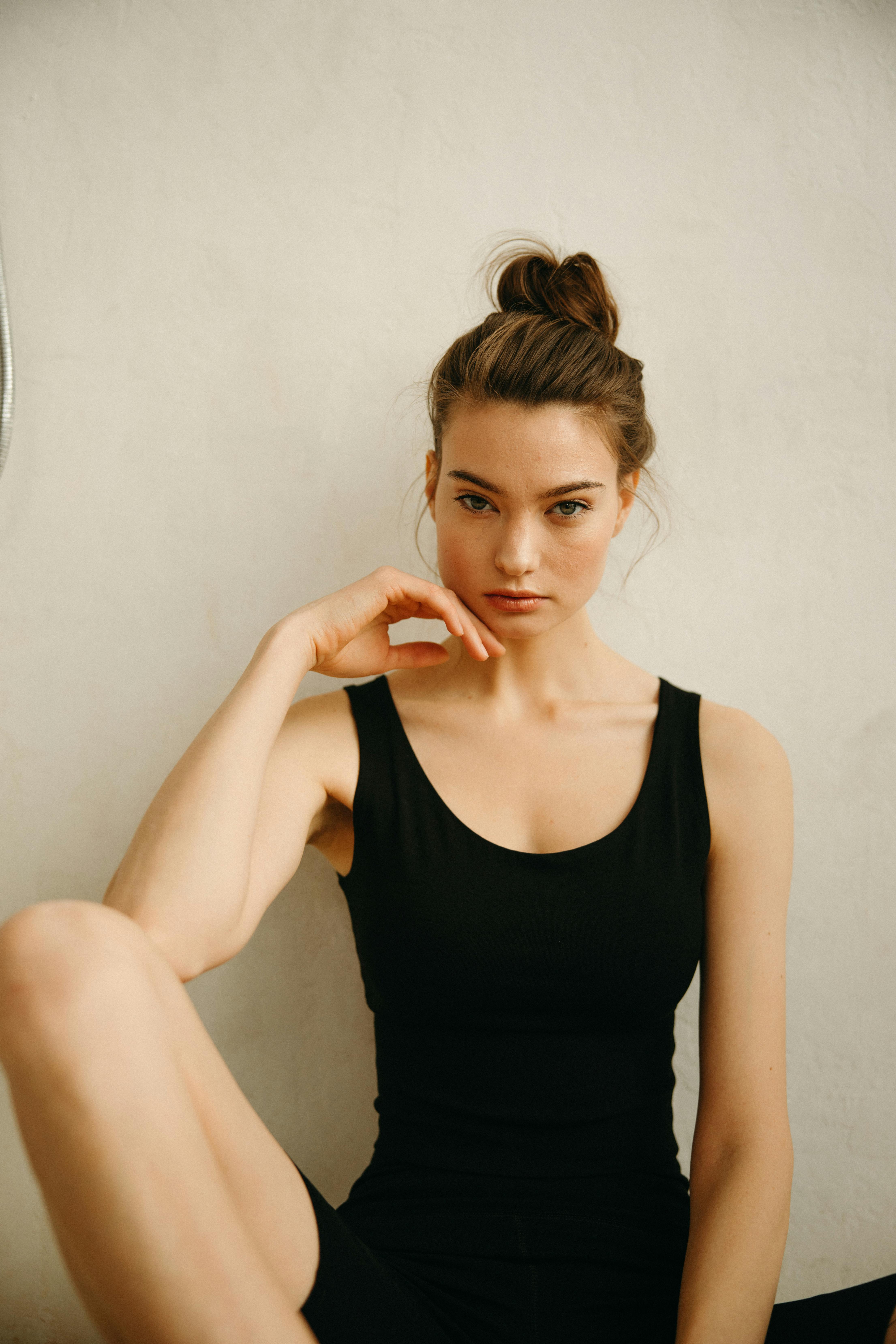 Confident woman with hand on face poses in a black outfit against a neutral background.