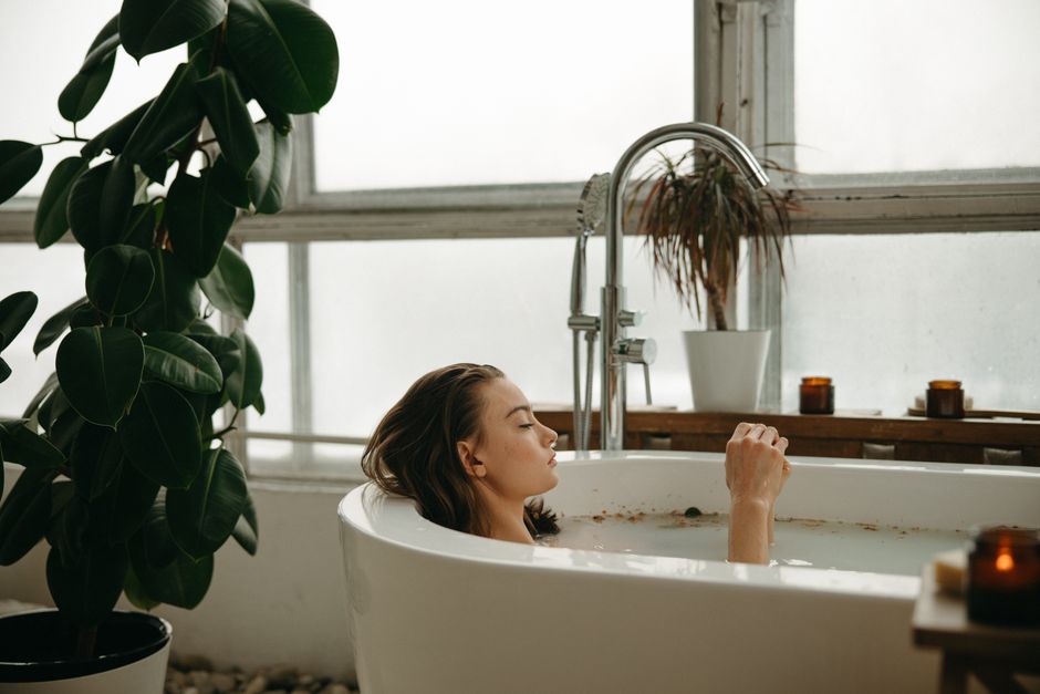 Como Criar um Ritual de Autocuidado para Mulheres Ocupadas 2 A woman peacefully soaking in a bathtub surrounded by plants and candles, embracing tranquility.