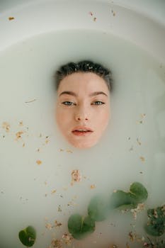 Woman's face submerged in a milky bath with petals, evoking tranquility and skincare rituals.