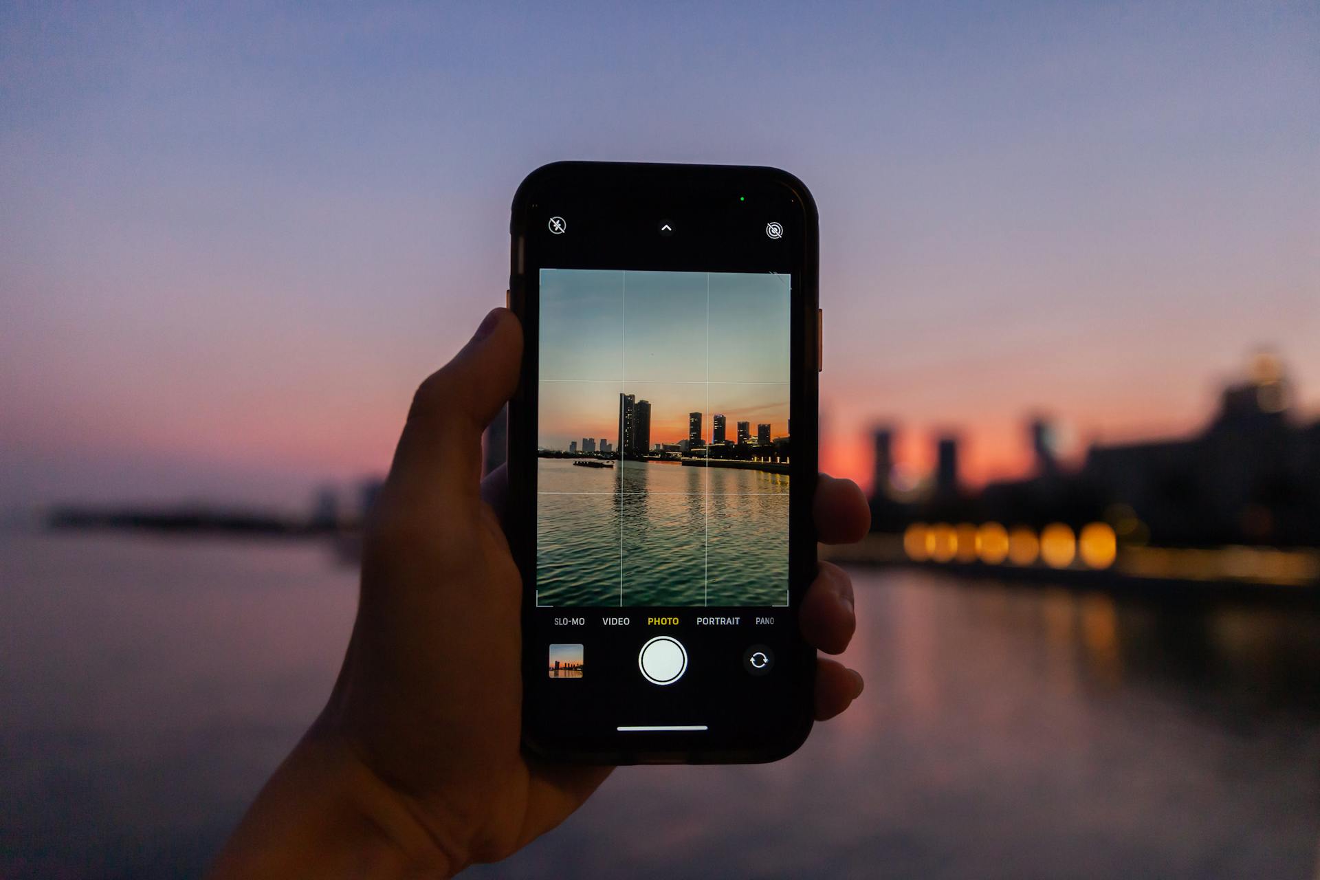 Hand holding smartphone capturing Shenzhen skyline during vibrant twilight.