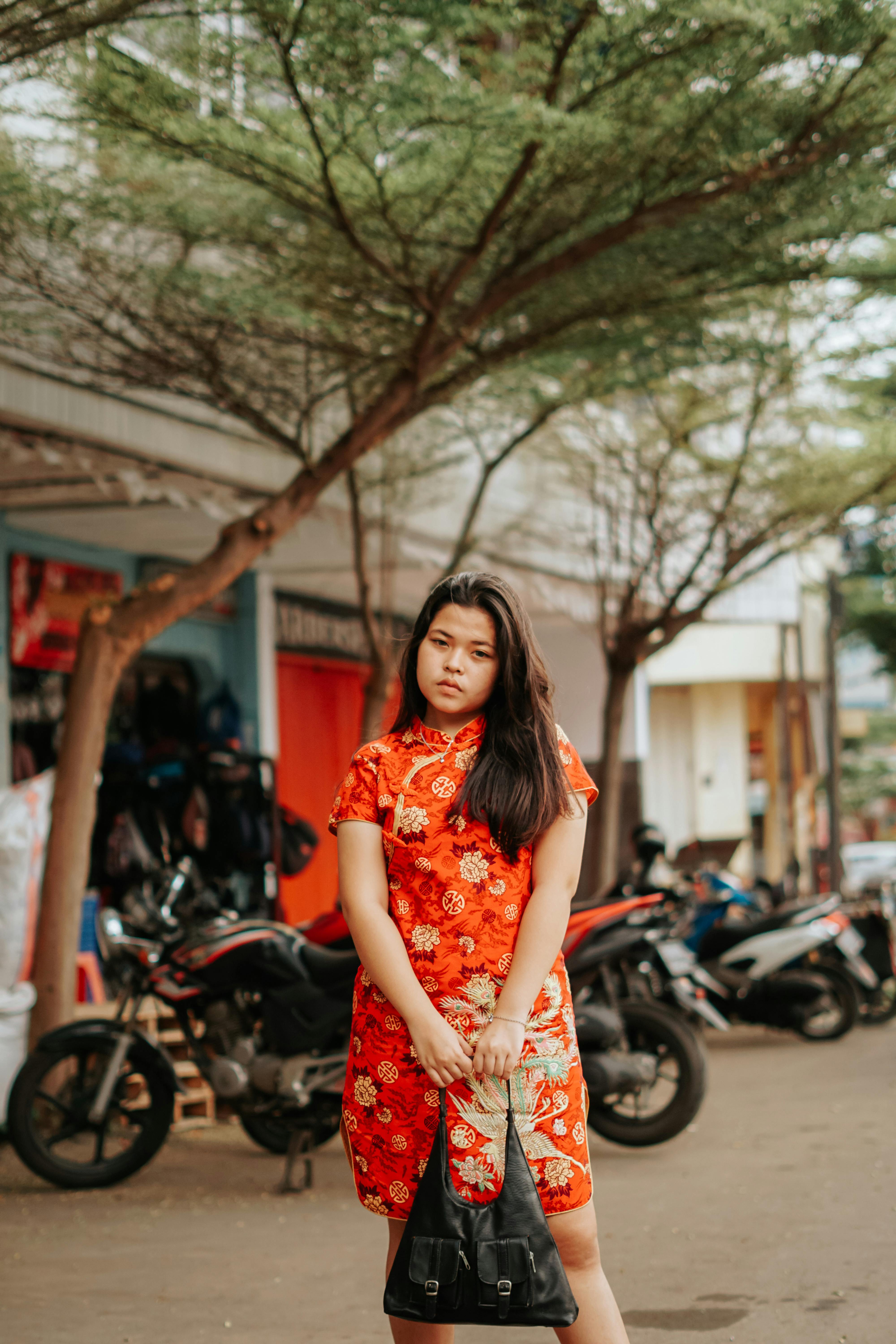 Free Child in red floral dress holding handbag in Cirebon, Indonesia. Trees and motorcycles in the background. Stock Photo