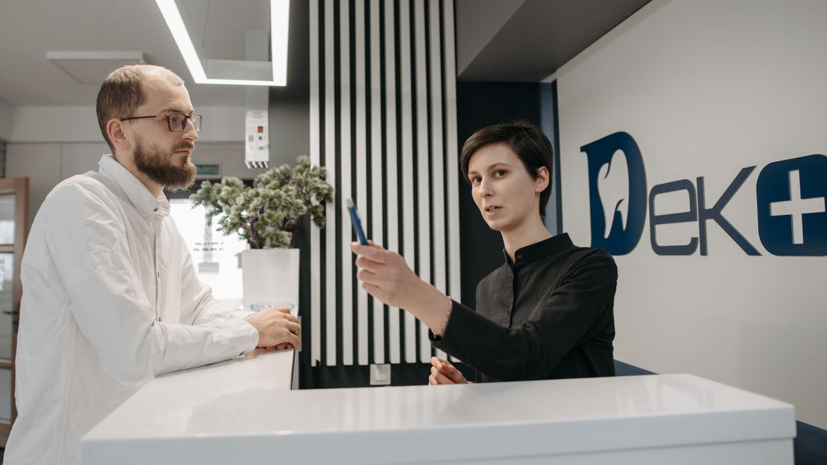 A man and a receptionist interacting at a dental clinic reception desk, showcasing customer service.