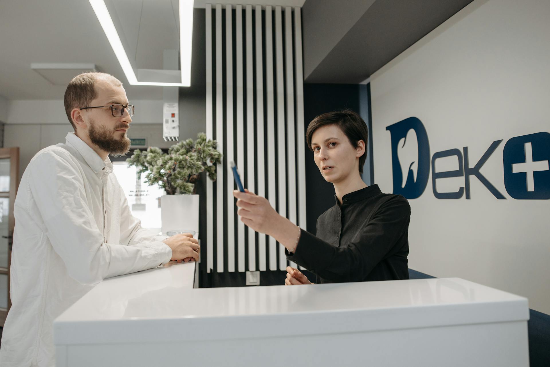 A man and a receptionist interacting at a dental clinic reception desk, showcasing customer service.