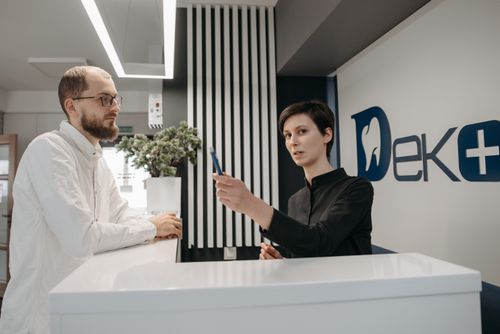 Free A man and a receptionist interacting at a dental clinic reception desk, showcasing customer service. Stock Photo