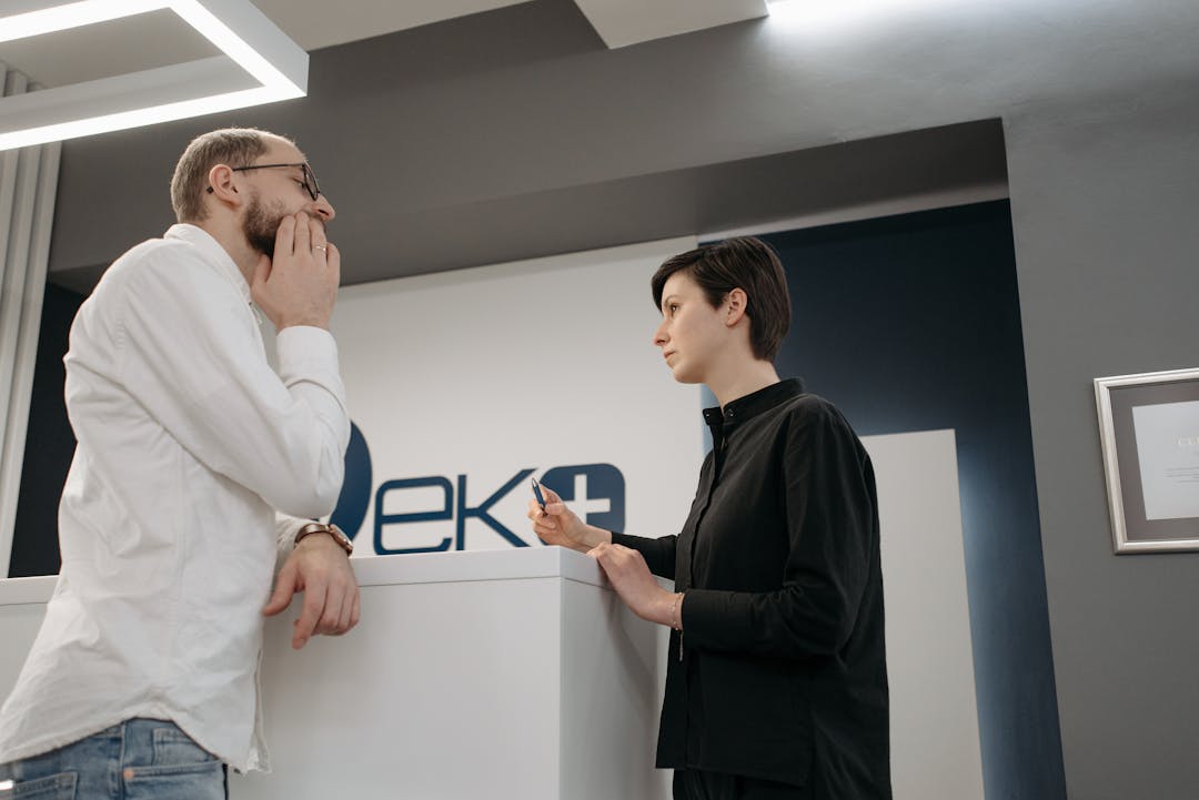 Two adults engaged in conversation at a modern office reception desk, highlighting professional customer service.