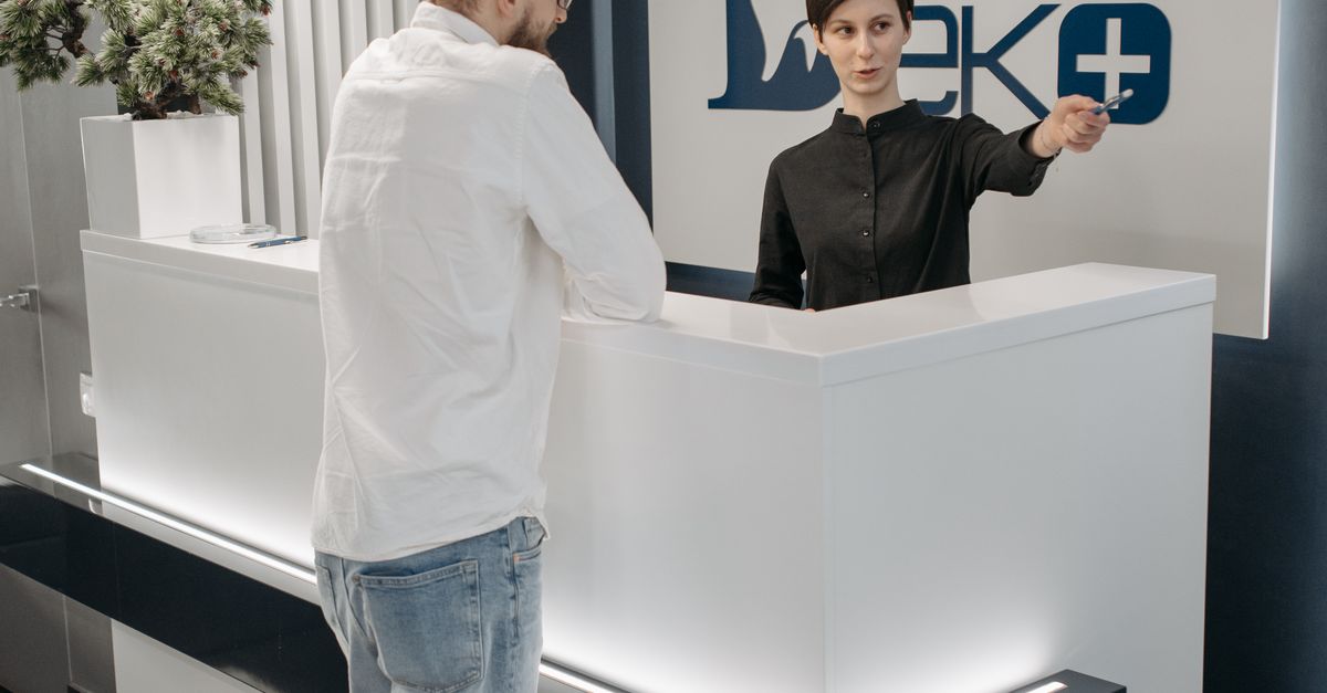 Modern dental clinic reception area with a receptionist assisting a patient.