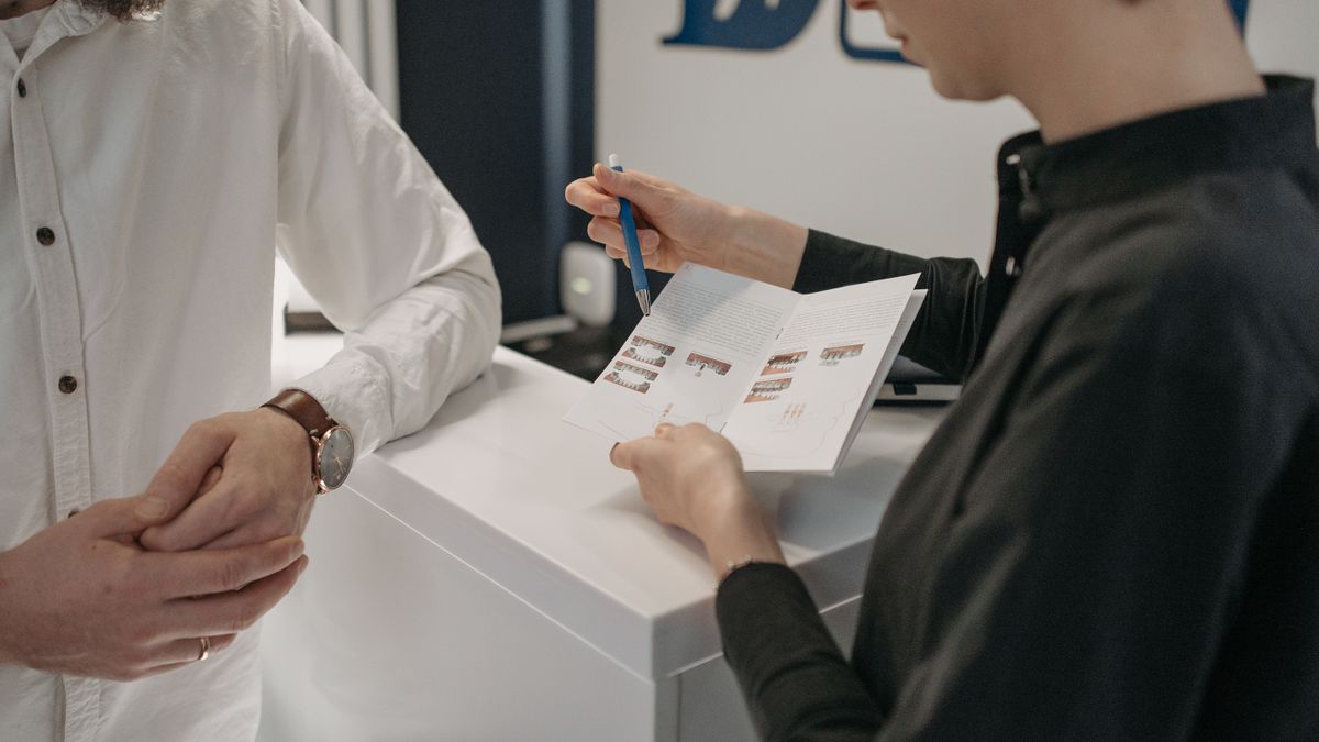 Reception staff explaining information to a customer at a clinic counter.