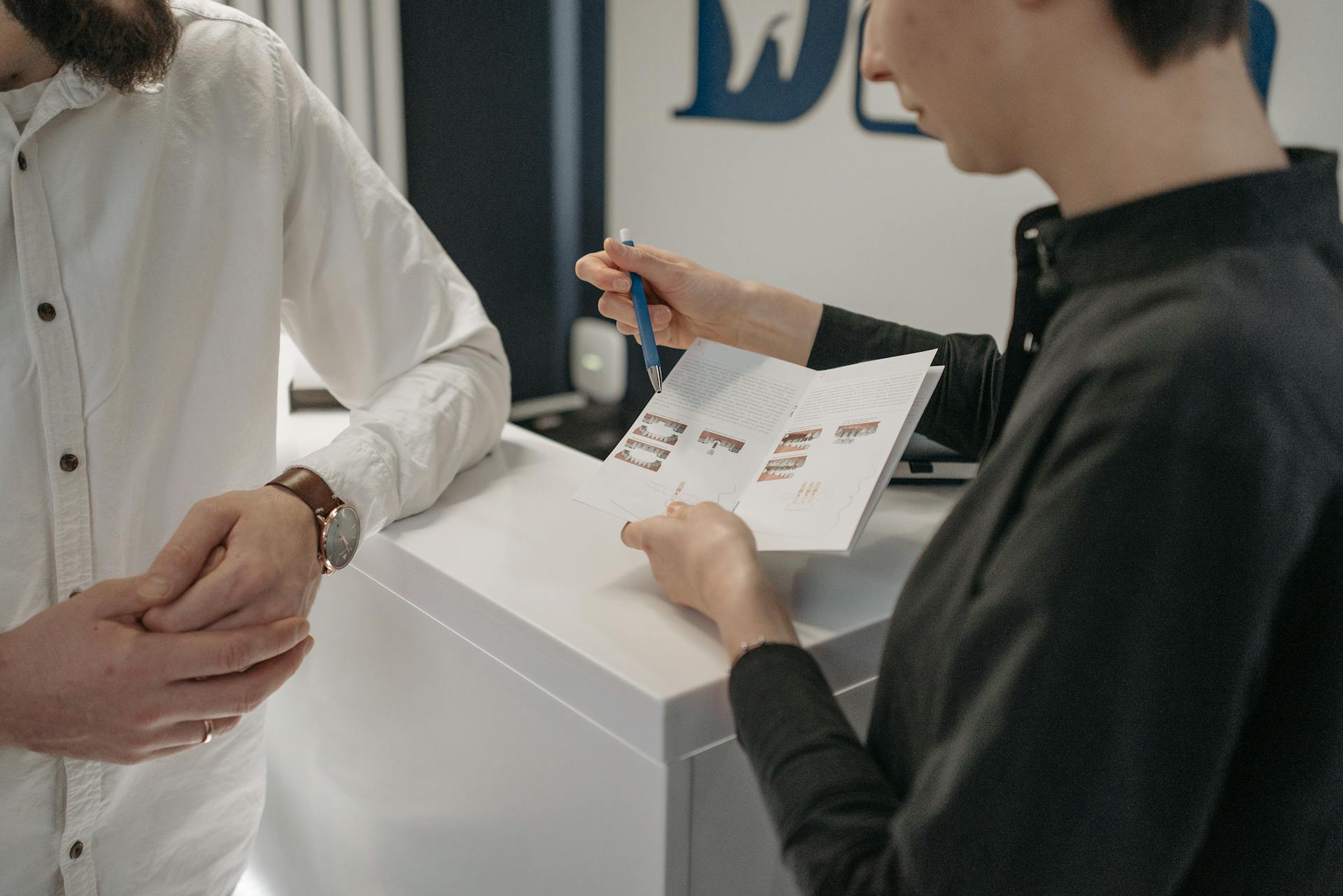 Reception staff explaining information to a customer at a clinic counter.