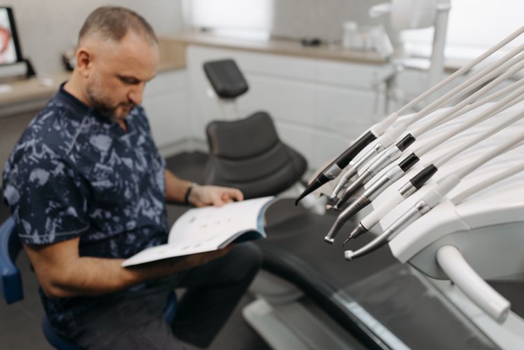 A male dentist reading a book in a modern dental clinic featuring advanced dental equipment.