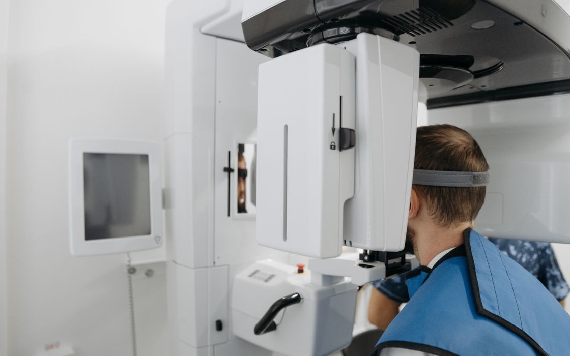 Patient standing in a panoramic dental X-ray machine wearing a protective lead apron