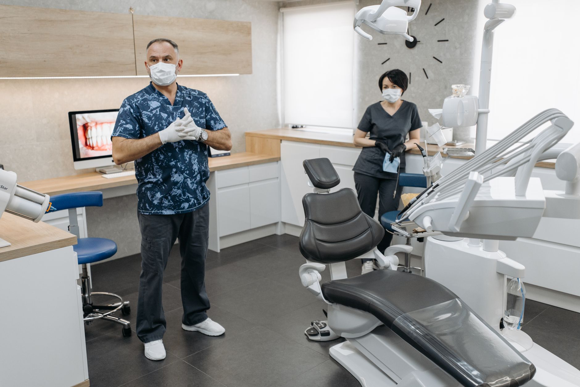 A dentist and assistant in a well-equipped modern dental clinic wearing masks and gloves.