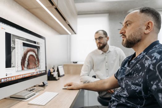 Two men discuss dental care at a computer, illustrating modern digital dentistry.