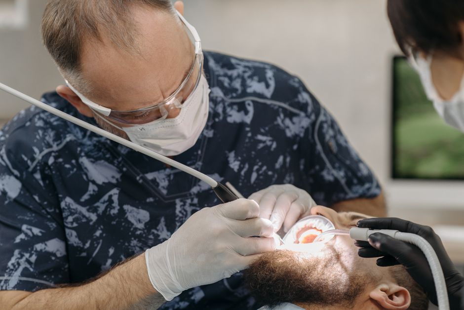 Dentist with instruments working on a patient's teeth in a clinical setting.
