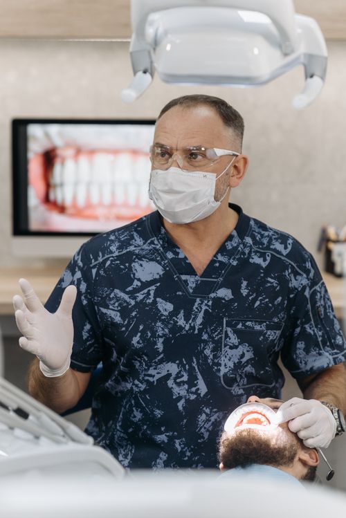 Free Dentist wearing protective gear examining a patient in a dental clinic with a screen displaying teeth. Stock Photo