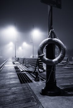 雾蒙蒙的夜晚，码头木板路上，救生圈和灯柱构成了一幅黑白的氛围场景