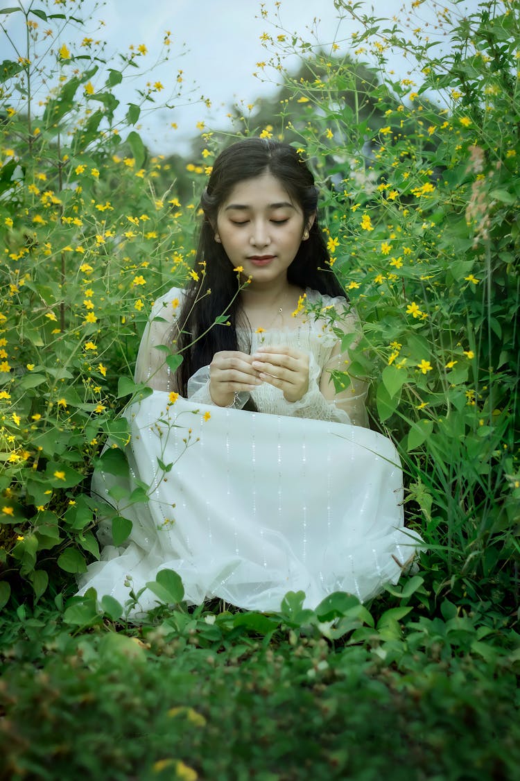 A Young Woman Sitting On The Ground Surrounded By Yellow Flowers