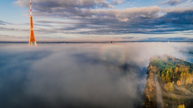 从空中拍摄，一座塔楼在云层上方升起，下方是风景秀丽的景观