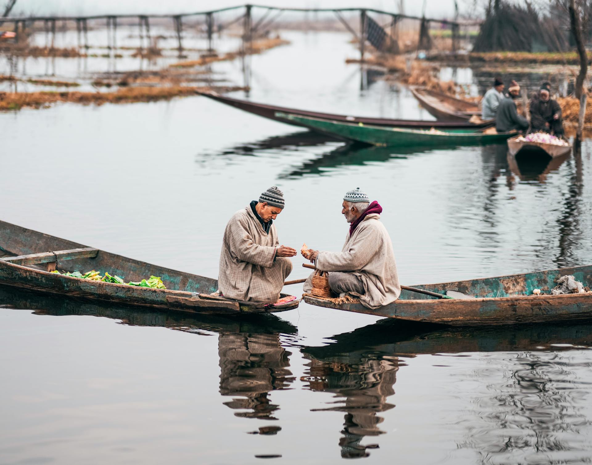 Two men trading goods on rustic boats at a tranquil lake, showcasing local commerce.