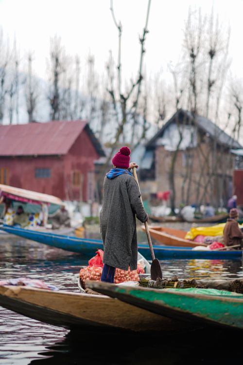 Free A traditional boatman rowing a canoe on a serene lake with colorful canoes and houses in the background. Stock Photo