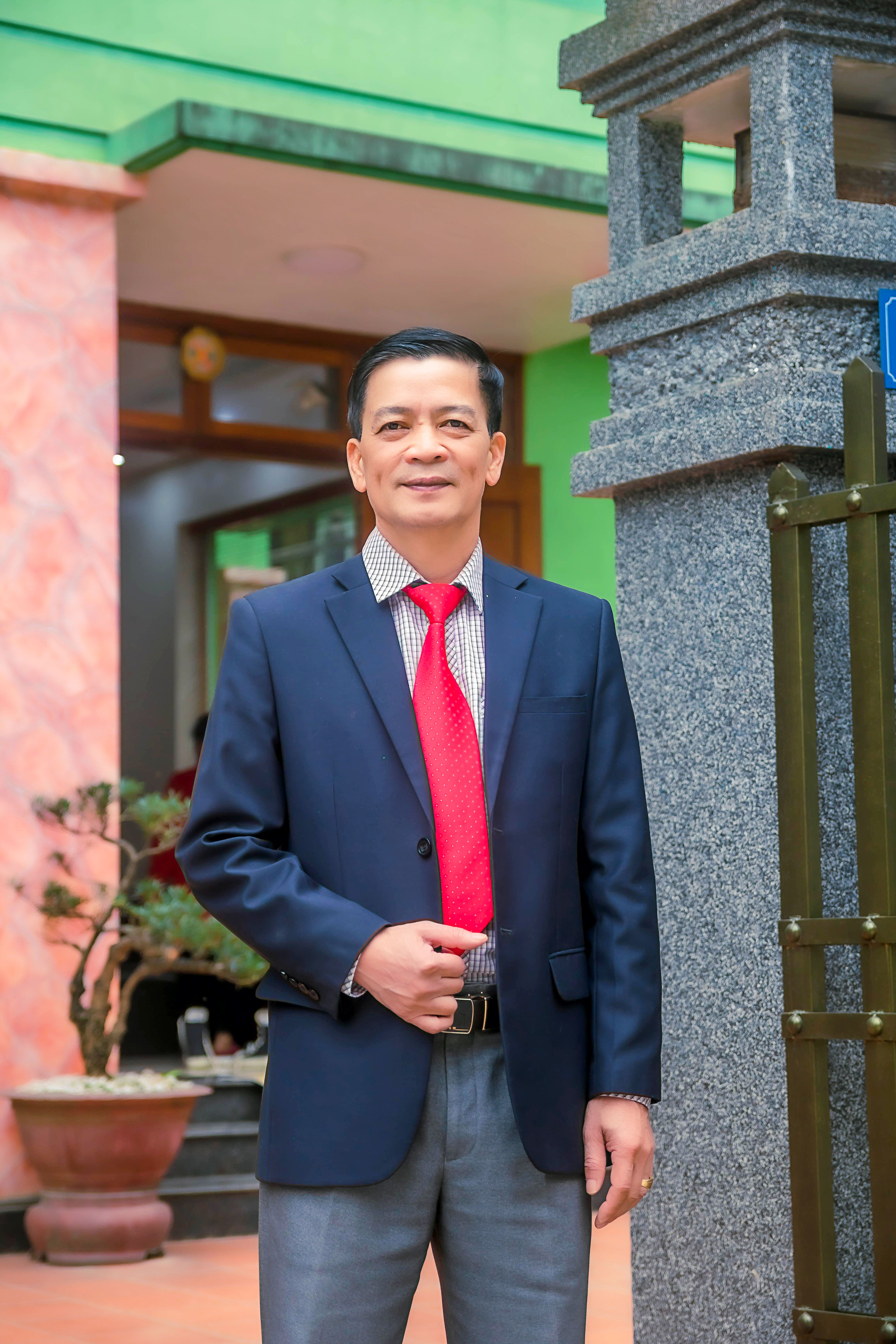 A confident businessman in a blue suit stands outdoors, posing with a smile.
