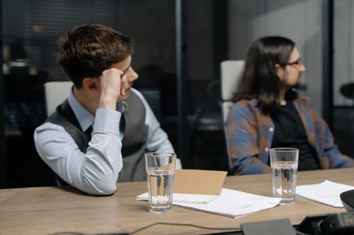 Free Two young adults in a business meeting setting with focus on written documents and water glasses. Stock Photo