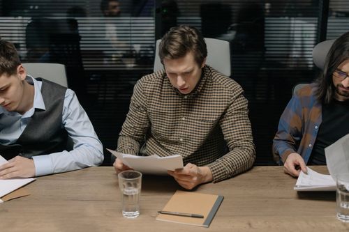 Free Three men reviewing papers in a modern office setting during a business meeting. Stock Photo