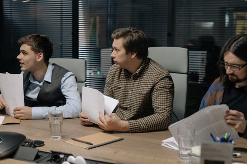 Free Three male colleagues engage in a business meeting discussing documents around a table. Stock Photo