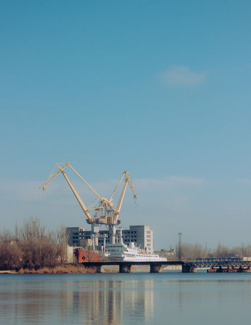 Free Modern construction crane located on shore of river near bridge against blue sky on autumn day in city Stock Photo