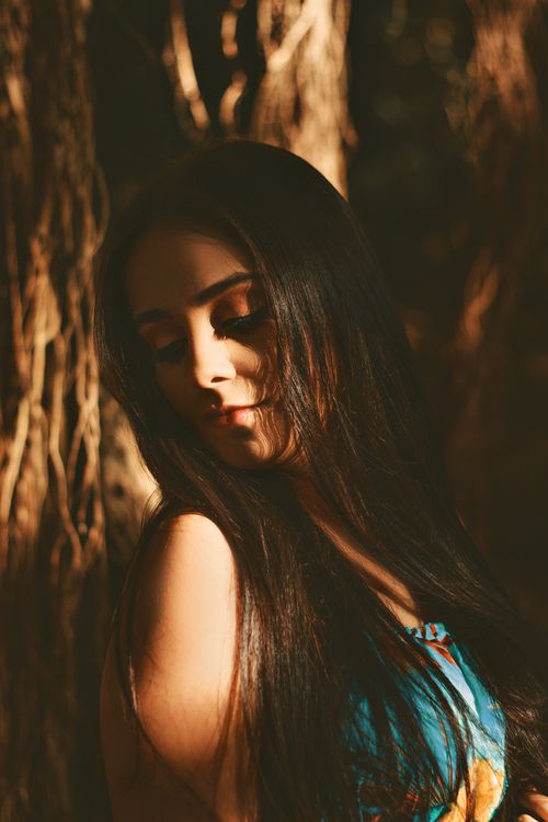 Free A serene portrait of a woman with long hair illuminated by natural light, set against an outdoor backdrop. Stock Photo