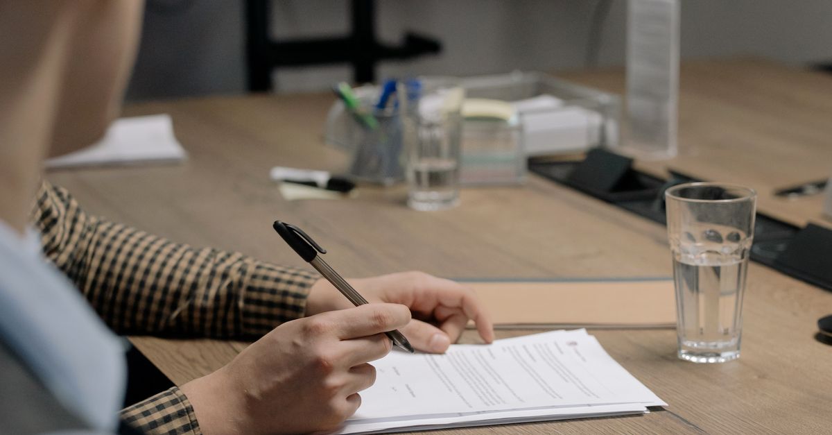 Pessoa de terno assinando um documento de contrato sobre uma mesa de madeira em escritório