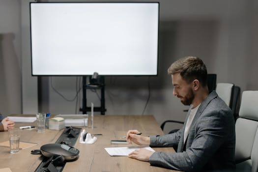 A professional businessman in a suit writing notes in an office meeting room during the day.