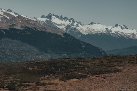 A breathtaking view of hikers on a trail amidst snow-capped mountains and expansive landscapes.